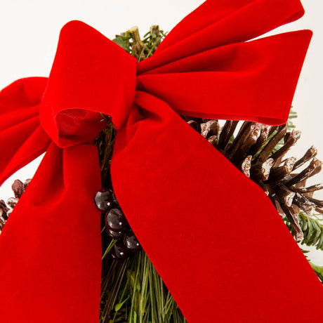 Close up of the red bow at the top of the wintergreen arrangement, giving a glimpse of the pine cones that are somewhat hidden between the bow and the Christmas greenery. 