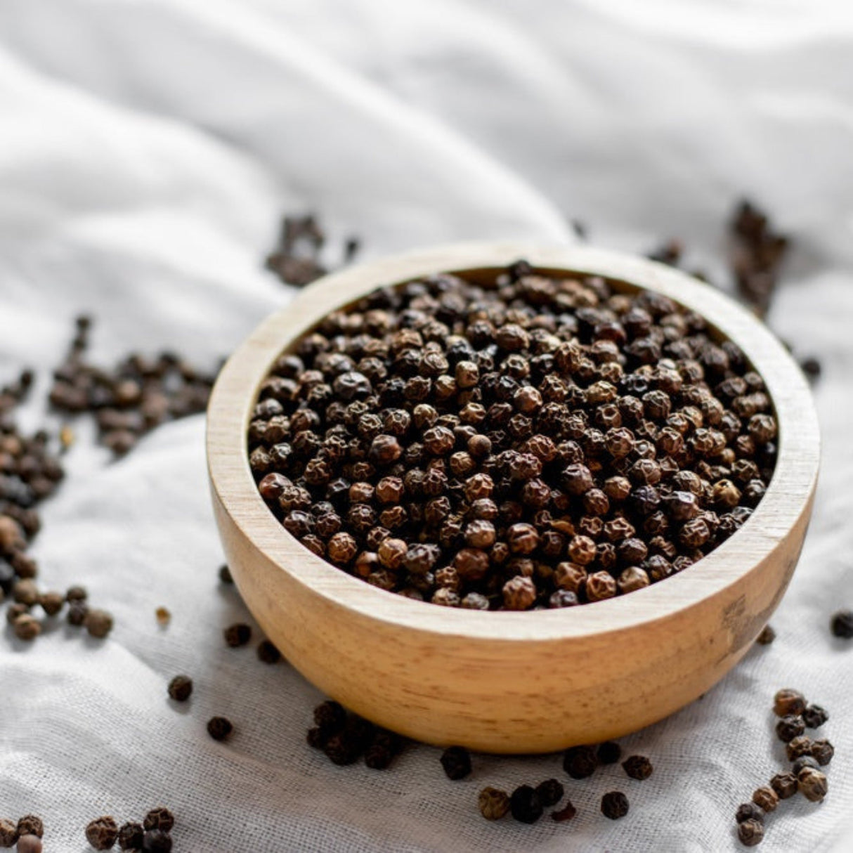 Wooden bowl filled with whole dried black peppercorns.