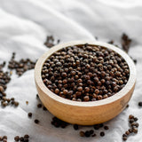 Wooden bowl filled with whole dried black peppercorns.