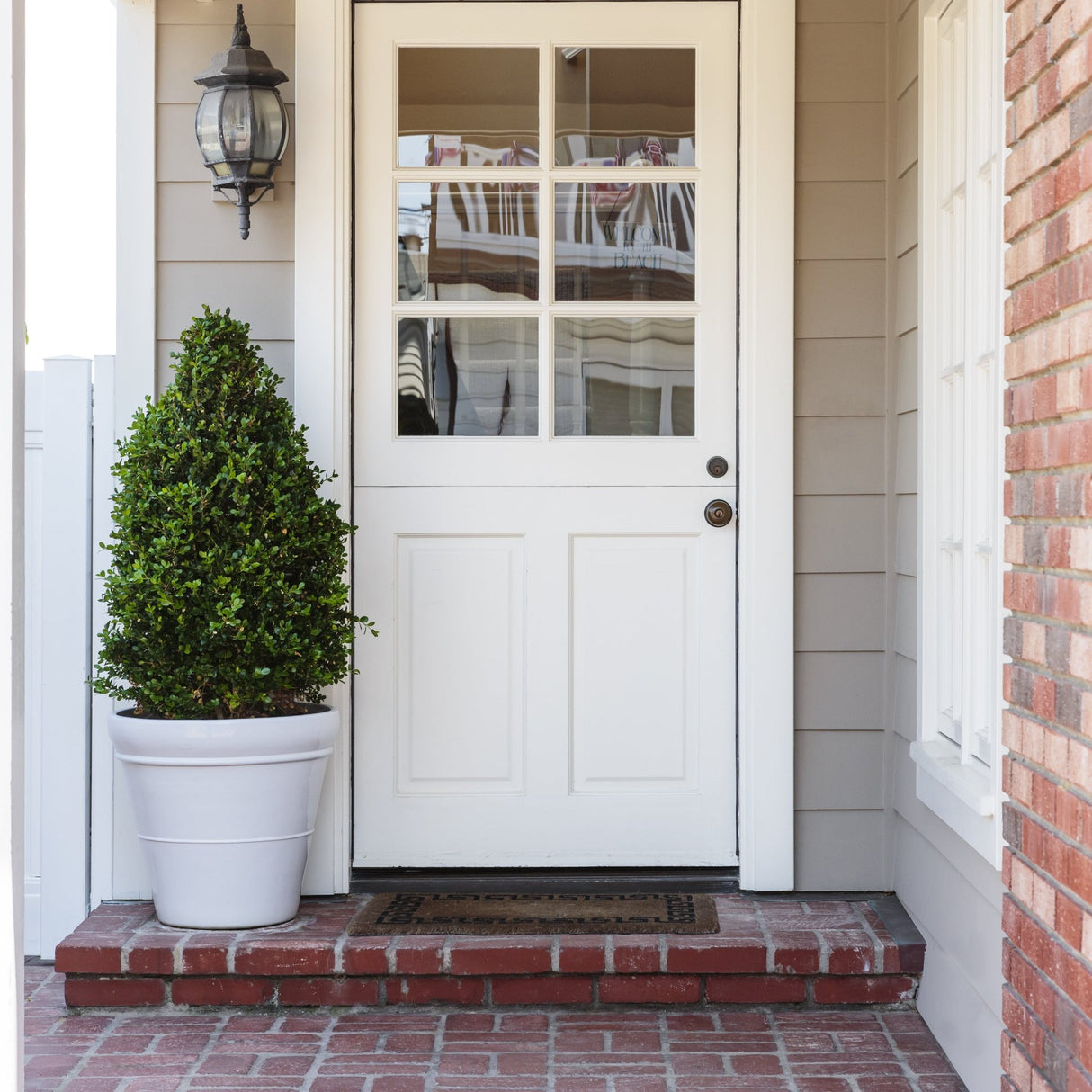 Boxwood cone in a white planter placed on a brick step in front of a white door with glass panes, creating a classic, welcoming entrance to the home.