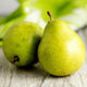 Two ripe green D'Anjou pears resting on a wooden surface with blurred background.